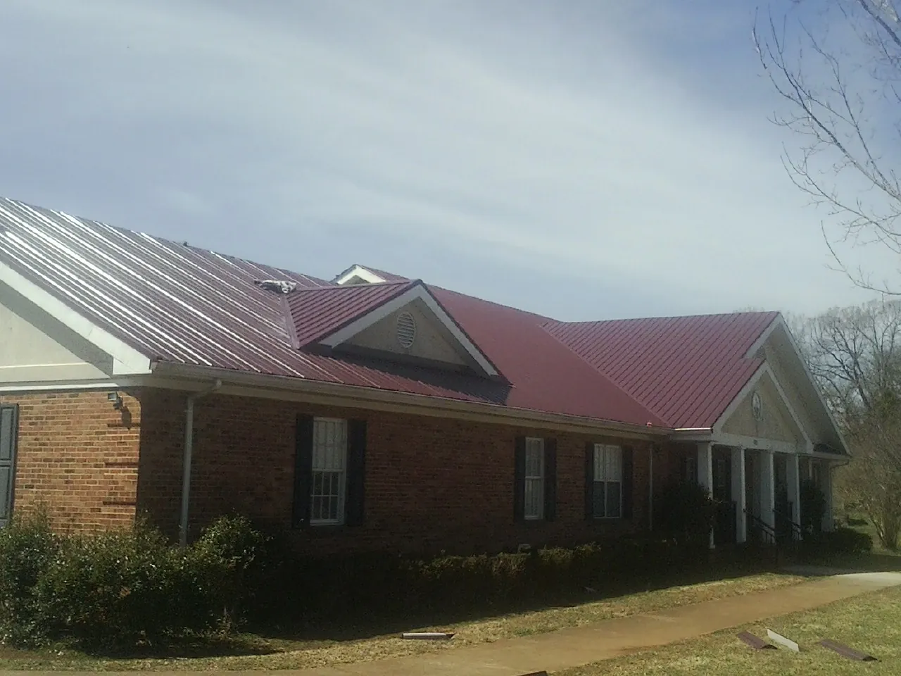 Red metal roof with gabled entries on a long brick building, from a Hail Damage Roof Repair job in Mc Henry