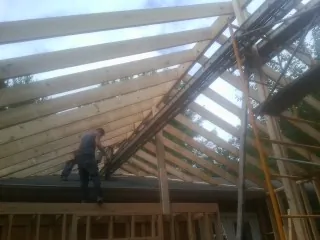 Rafters going up over a new addition with a worker on the wall in Mc Henry
