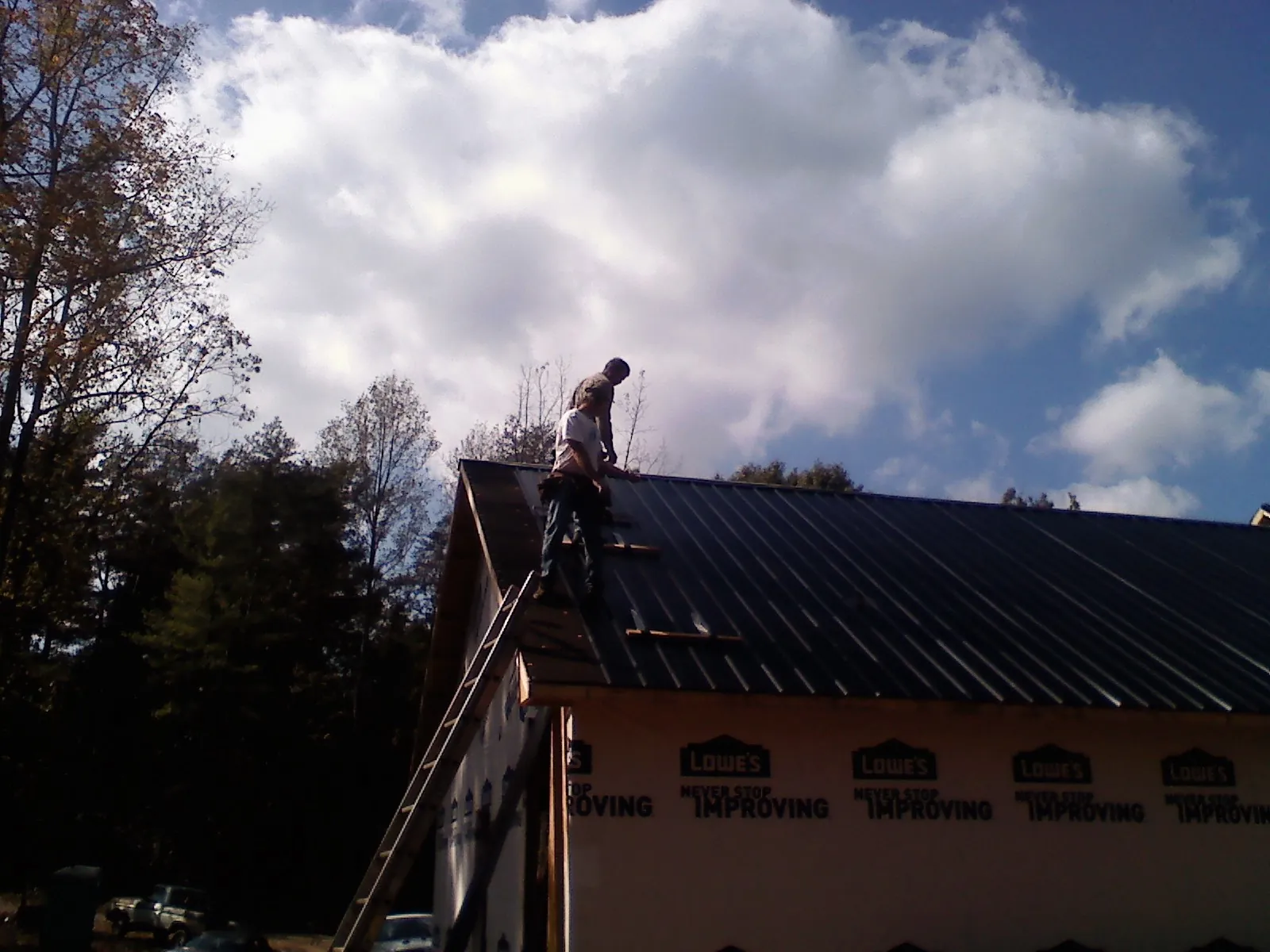 Roofer fastening dark metal panels high against a cloudy sky, from a Roof Inspection job in Mc Henry